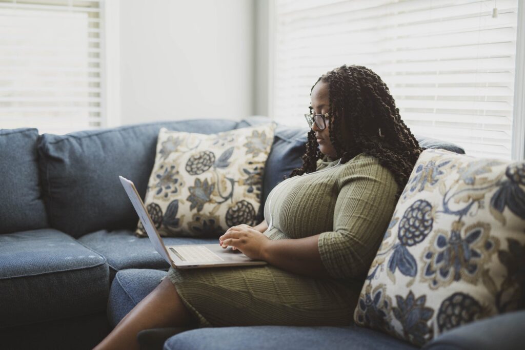 Woman sitting on a couch at home researching therapists on a laptop