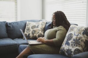 Woman sitting on a couch at home researching therapists on a laptop